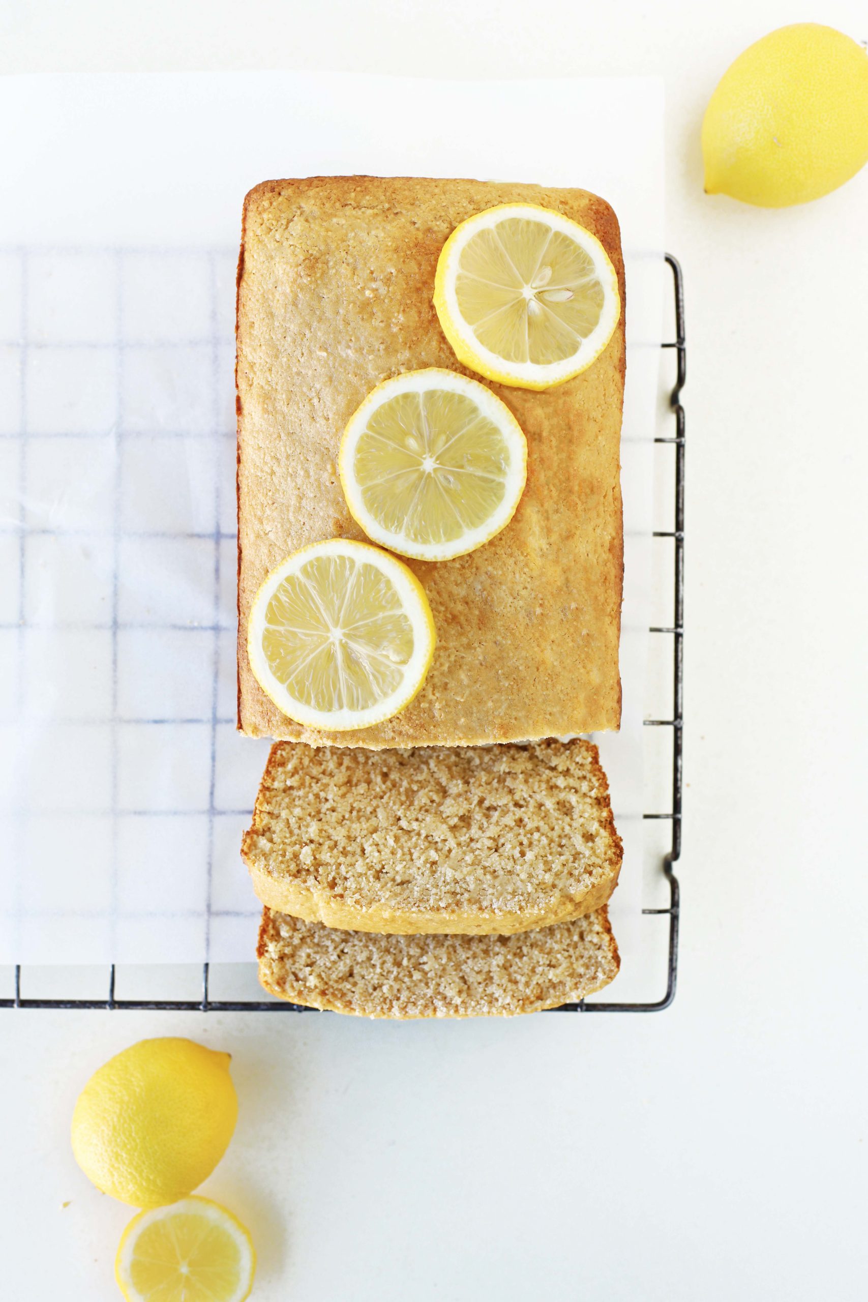Healthy, fluffy and moist vegan lemon loaf cake slice on a cooling rack with fresh lemon