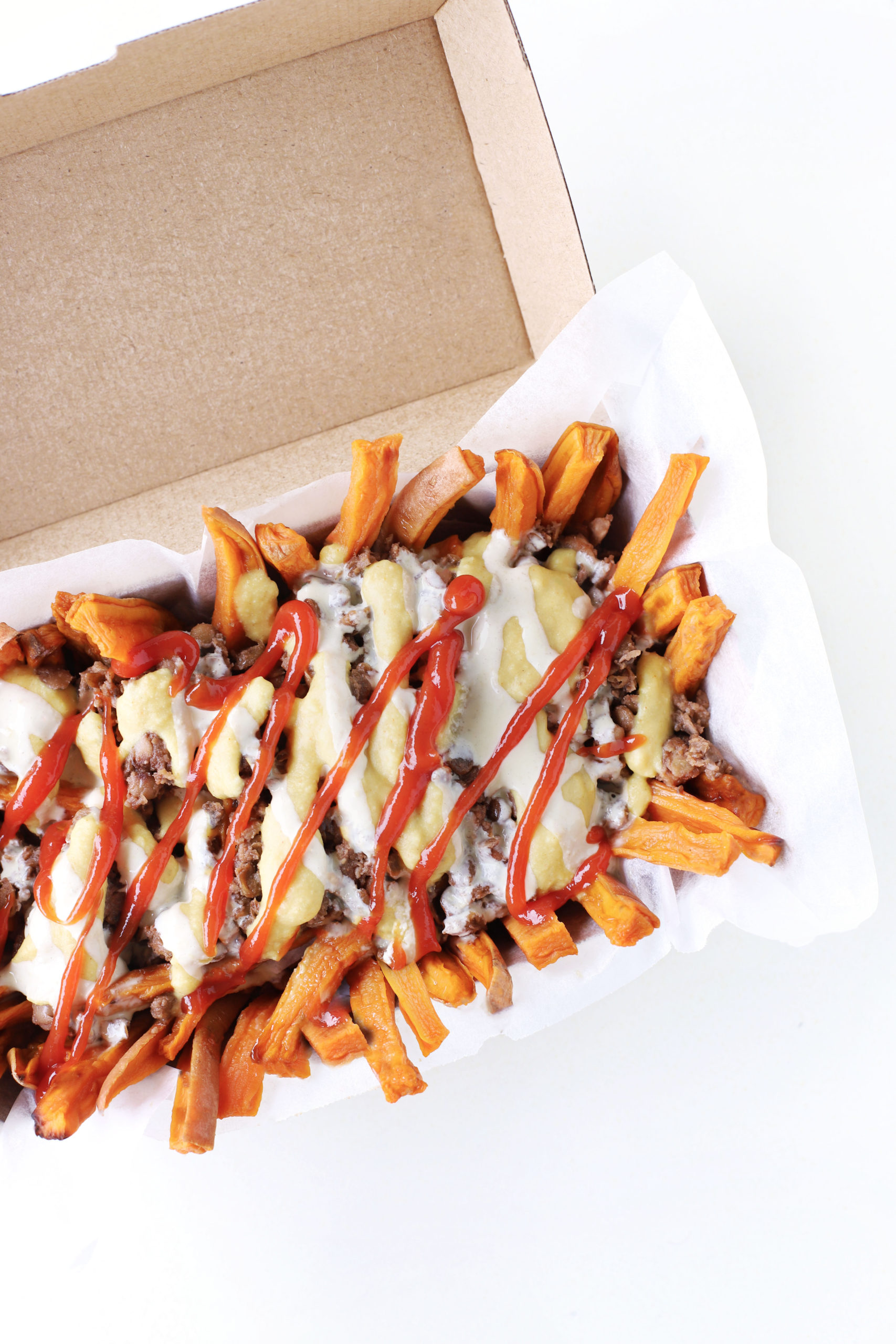 Healthy Vegan sweet potato fries poutine with creamy hummus sauce, ketchup (tomato sauce) plantbased 'mince' meat and dairy free cheesy sauce.