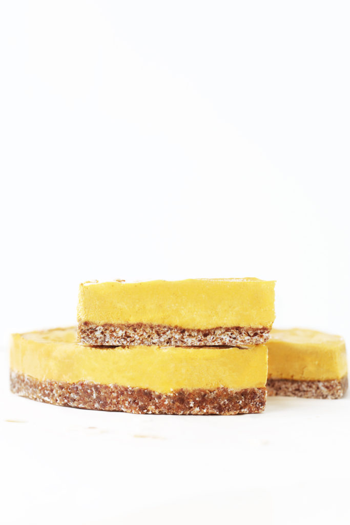 Slices of healthy dairy free pumpkin cheesecake with a chewy date crust base stacked on top of eachother
