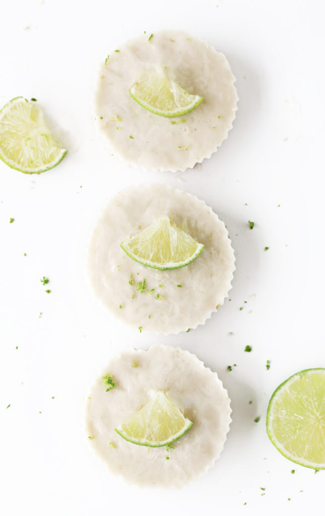 3 mini vegan key lime pies lined up in a row with fresh lime wedges and lime zest. A simple gluten free coconut condensed milk pie with sweet and salty raw vegan pie crust