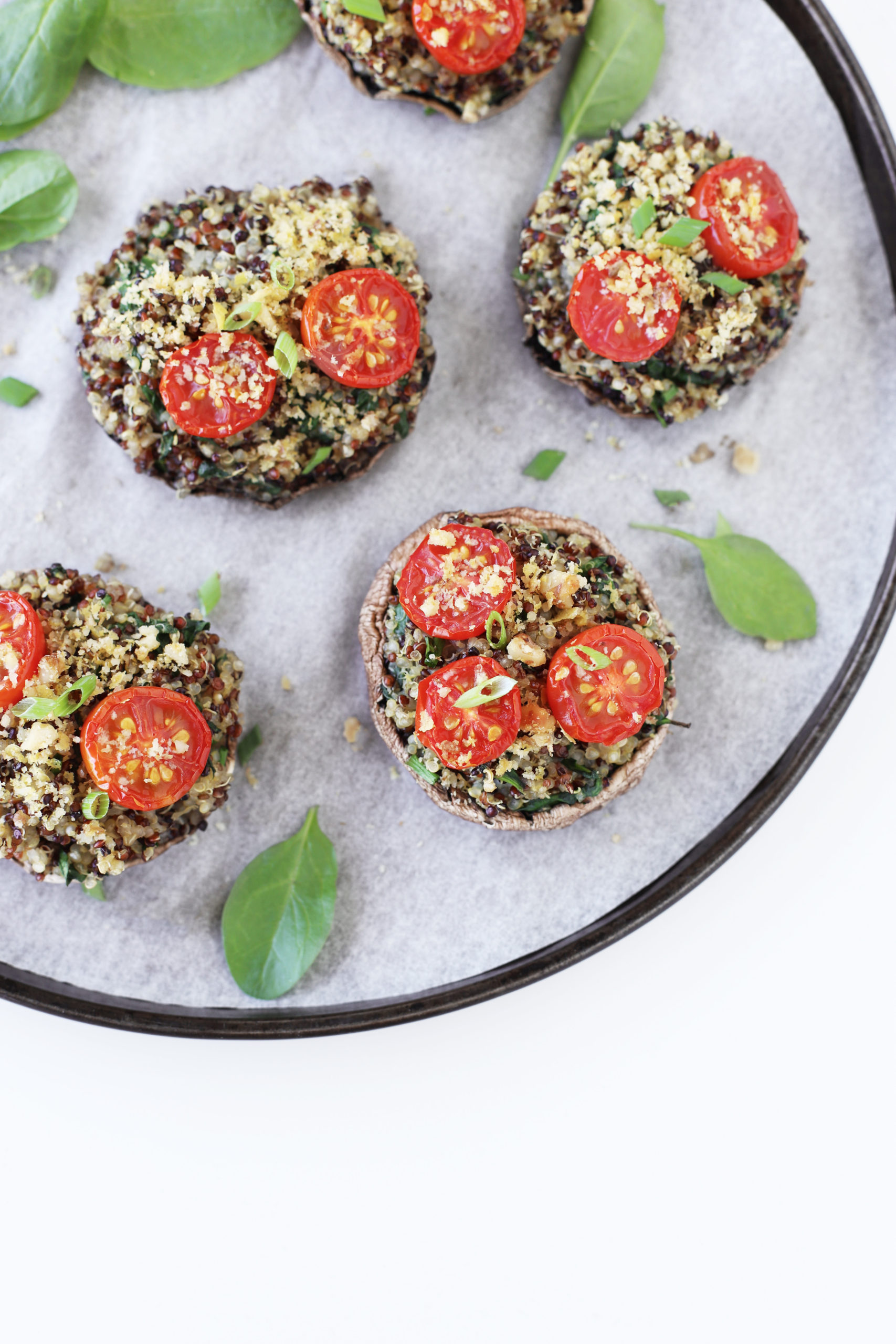 Baked vegetarian stuffed portobello mushrooms filled with quinoa, spinach, roasted tomatoes and herbs with a crunchy walnut parmesan crumble topping, lying on a baking tray.
