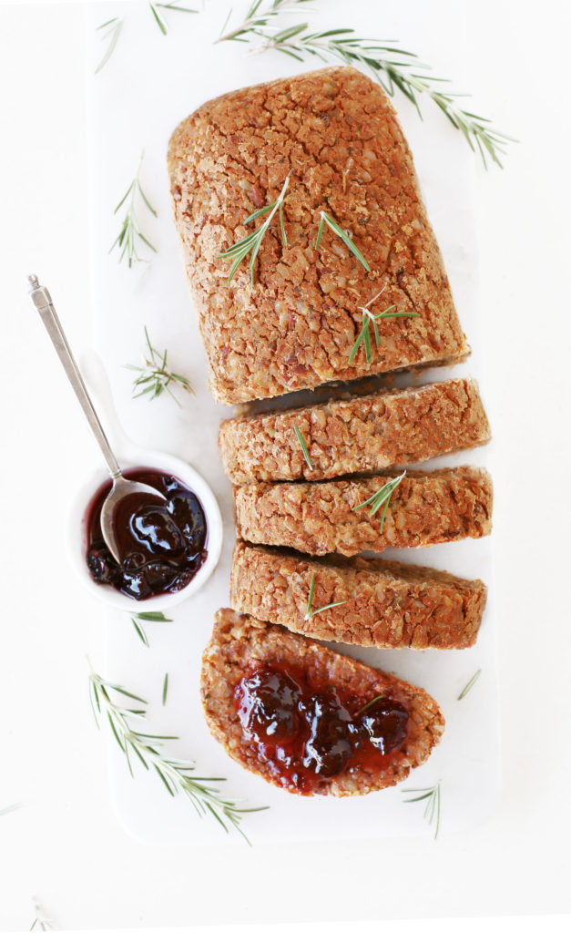 Vegan nut (free) roast loaf sliceson white marble platter with cranberry sauce and fresh rosemary