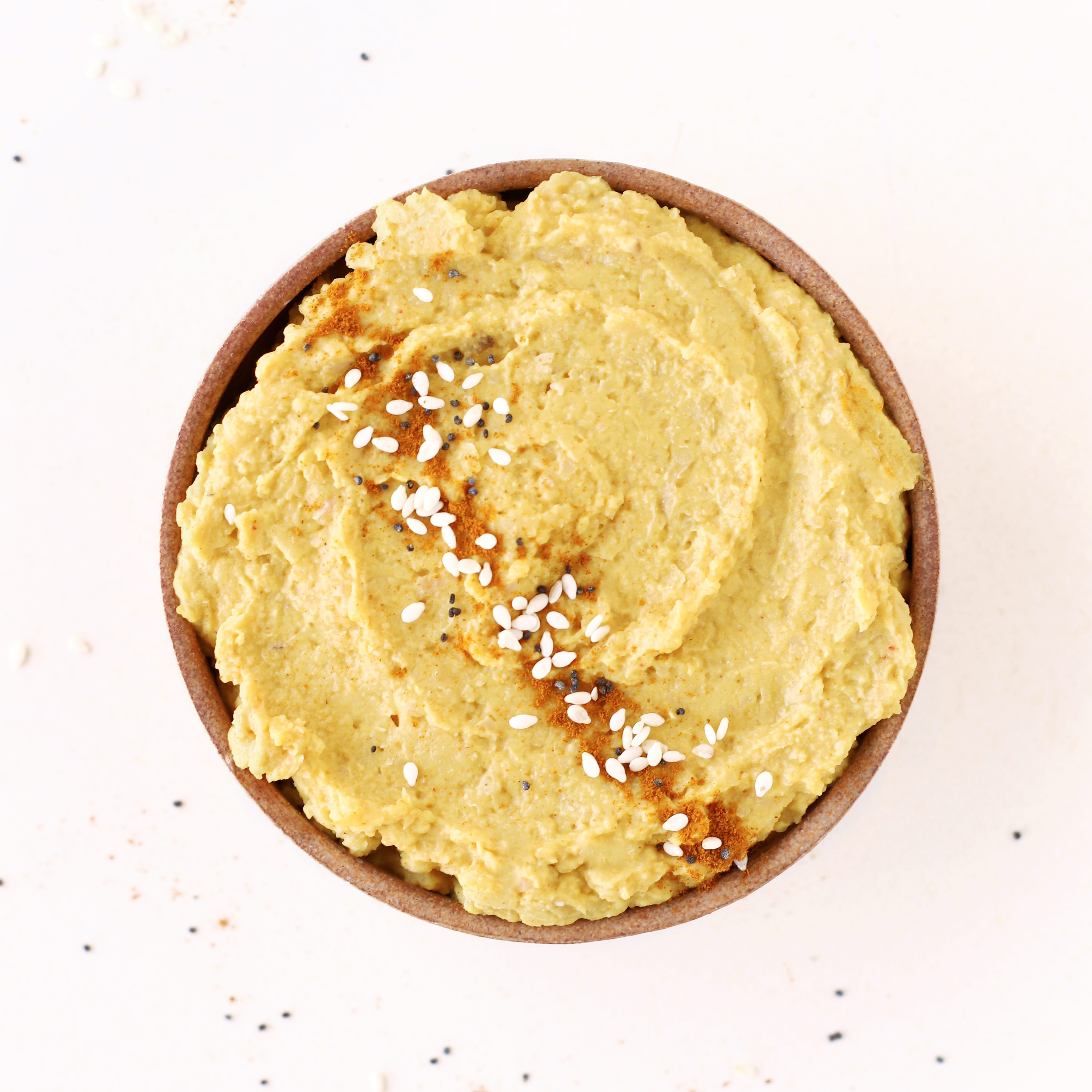 bowl of healthy yellow turmeric spiced oil free creamy hummus topped with sesame seeds paprika