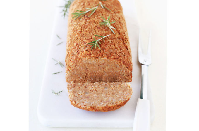 Vegan nut (free) vegetarian roast loaf on white marble platter with cranberry sauce and fresh rosemary